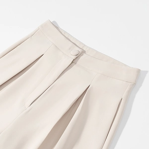 Detail van de crèmekleurige broek met hoge taille, plooien aan de voorkant en stoffen knoop