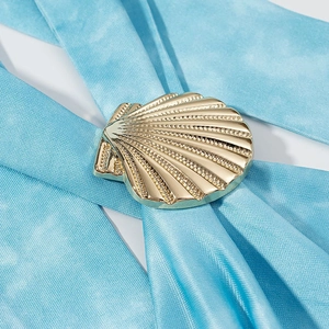Golden shell-shaped metal buckle on light blue fabric showing polished striped detail