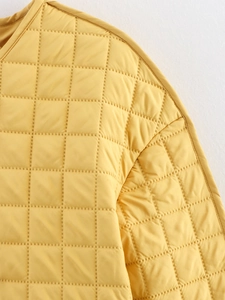 Detail of yellow quilted jacket showing precision stitching and square pattern texture