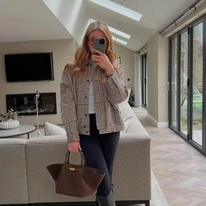Women's plaid bomber jacket in brown tones paired with a minimalist leather handbag