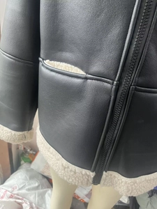 Detail of black faux leather jacket with white shearling lining and metal zipper closure
