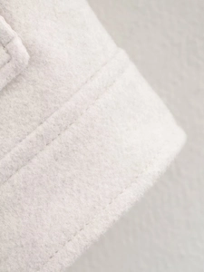 Detail shot of off-white tweed texture and premium double-stitching on the jacket sleeve