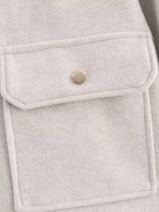 Macro shot of light gray tweed texture with rectangular flap pocket and gold metal button