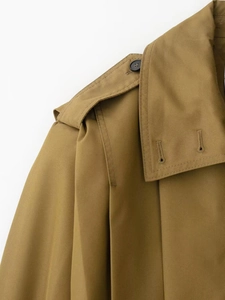 Detail of khaki trench coat featuring shoulder epaulettes and classic brown buttons