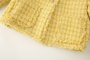 Détail du tissu en tweed jaune avec bordures effilochées et bouton doré élégant