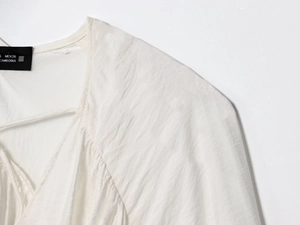 Close-up of white v-neck blouse showing detailed pleats and premium linen texture