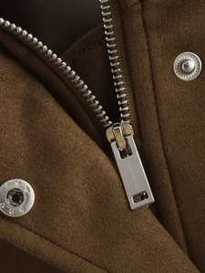 Détail de la fermeture éclair argentée et bouton-pression sur veste marron en faux daim