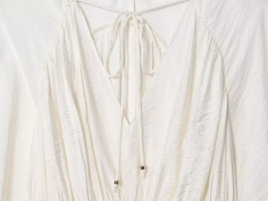 Detailed view of deep V-neckline with silver-tipped ties on a white textured blouse
