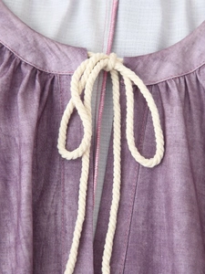Detail of linen texture fabric with cream hemp rope tie at the purple tunic neckline