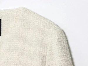 Detailed close-up of textured tweed fabric with elegant metal buttons and crew neckline