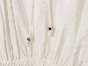 Detailed close-up of white pleated fabric with adjustable drawstrings and silver beads
