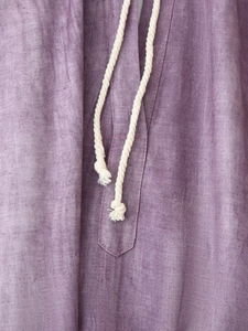 Detail of purple linen dress featuring a V-neckline with cream braided drawstrings and tassels