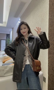 Detail view of a black faux leather jacket paired with a brown croc-effect H-buckle bag