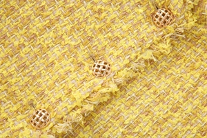 Détail de la texture en tweed jaune avec bords frangés et boutons dorés travaillés