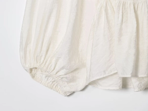 Detail of white pleated blouse featuring elastic cuffs and textured fabric finish