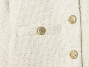 Detail of ivory tweed fabric with golden embossed crest buttons and flat pocket stitching