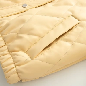 Detail of yellow quilted faux leather jacket featuring silver snaps and elastic hem