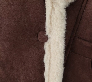 Detailed close-up of brown suede jacket with cream sherpa trim and fabric-covered button
