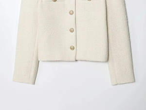 Detailed close-up of vintage gold buttons on a white tweed jacket with woven texture