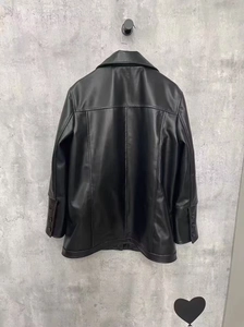 Rear view of black glossy leather jacket with buttoned cuffs and industrial gray background