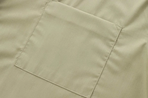 Detailed close-up of pocket stitching and smooth poplin fabric texture on khaki shirt