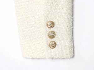 Close-up of white tweed fabric texture with three golden embossed vintage buttons