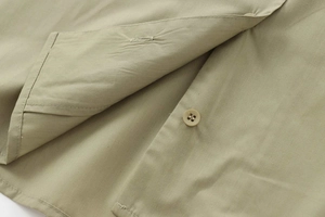 Close-up of tonal button and detailed stitching on olive poplin shirt fabric