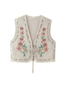 Detail of floral embroidery and white lace trim on a light beige cotton vest for women
