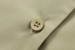 Detailed macro view of high-quality sage green poplin fabric and matching four-hole resin button