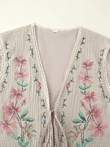 Close-up of floral cross-stitch embroidery and lace trim on the beige cotton vest