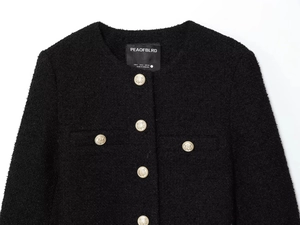 Detailed close-up of a black tweed jacket with gold metal buttons and brand label