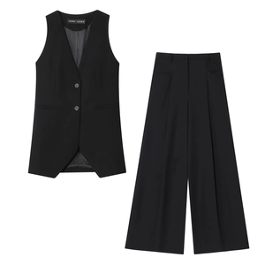 Détail du gilet noir à col en V et du pantalon large avec des plis marqués