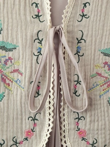Close-up of cotton floral cross-stitch embroidery with lace trim and tie detail