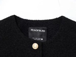 Detail of the golden crest button and woven tweed texture on the black French jacket