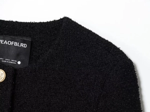 Detailed close-up of premium black tweed jacket with ornate gold anchor button and brand label