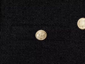 Close-up of black tweed fabric texture with decorative gold embossed nautical buttons