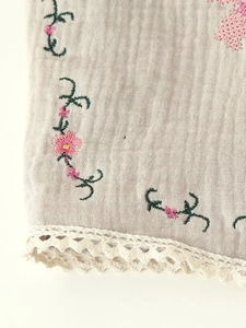 Detail of floral embroidery and white crochet lace trim on beige cotton vest fabric