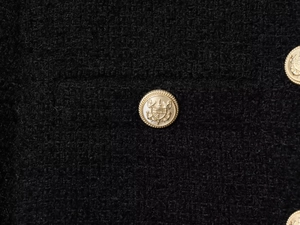 Detail of golden crest buttons on black tweed jacket featuring intricate woven texture