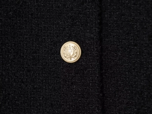 Close-up of golden metal crest button on premium black tweed jacket fabric