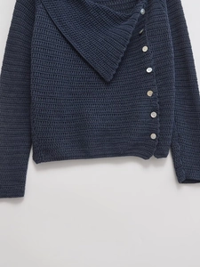 Detail of dark knit cardigan featuring asymmetric lapels and pearlized white buttons
