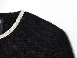 Macro detail of black tweed jacket featuring white braided trim and textured weave fabric
