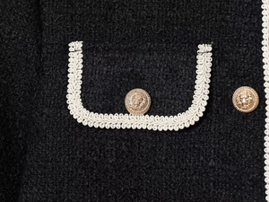 Macro detail of black tweed jacket featuring white braided trim and lion head gold buttons