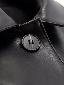 Close-up of black faux leather texture with detailed lapel and striped button detail