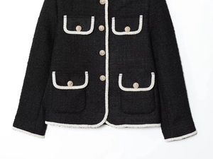Detailed view of black tweed jacket with white braided trim and ornate gold buttons