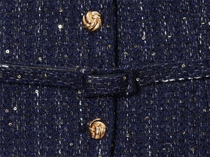 Close-up of dark blue tweed fabric with gold sequins and stylish knot-shaped buttons