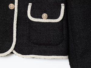 Macro detail of black tweed jacket with white braided trim and gold lion embossed button