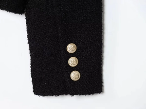 Detailed macro view of black bouclé jacket cuff with three embossed gold metal buttons