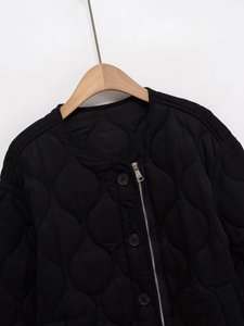 Detail of black quilted jacket with wave patterns, crew neck and dual zip button closure