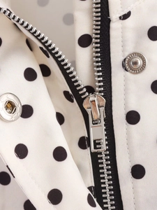 Detail of silver metal zipper and snap buttons on a white jacket with black polka dots