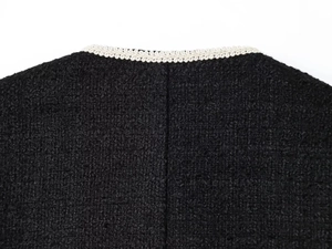 Close-up of black boucle jacket showing textured weave and white braided trim details